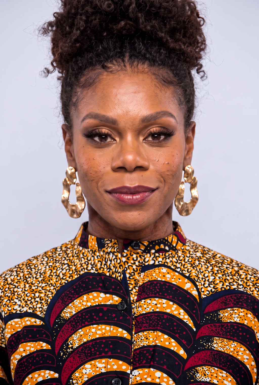 A close-up portrait of a woman  wearing a vibrant yellow, black, and red patterned Ankara shirt  dress 