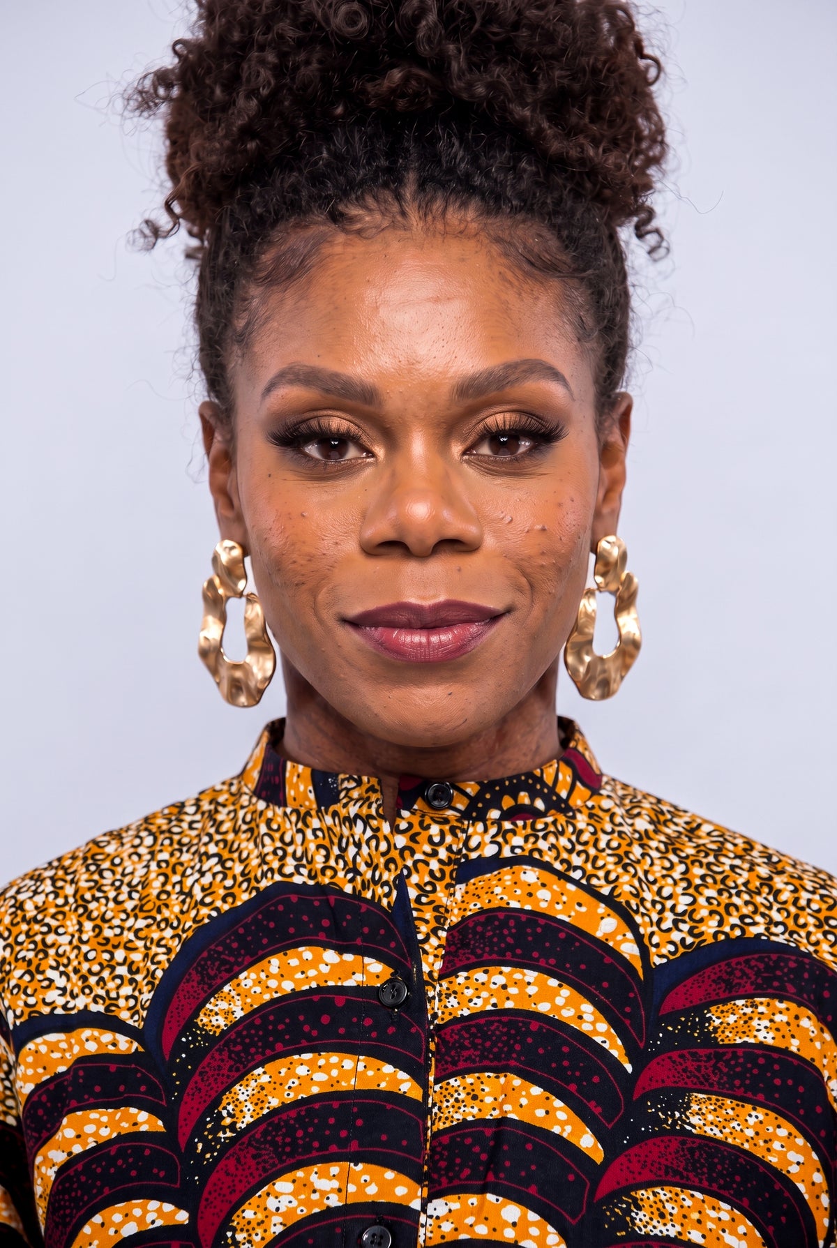 A close-up portrait of a woman  wearing a vibrant yellow, black, and red patterned Ankara shirt  dress 