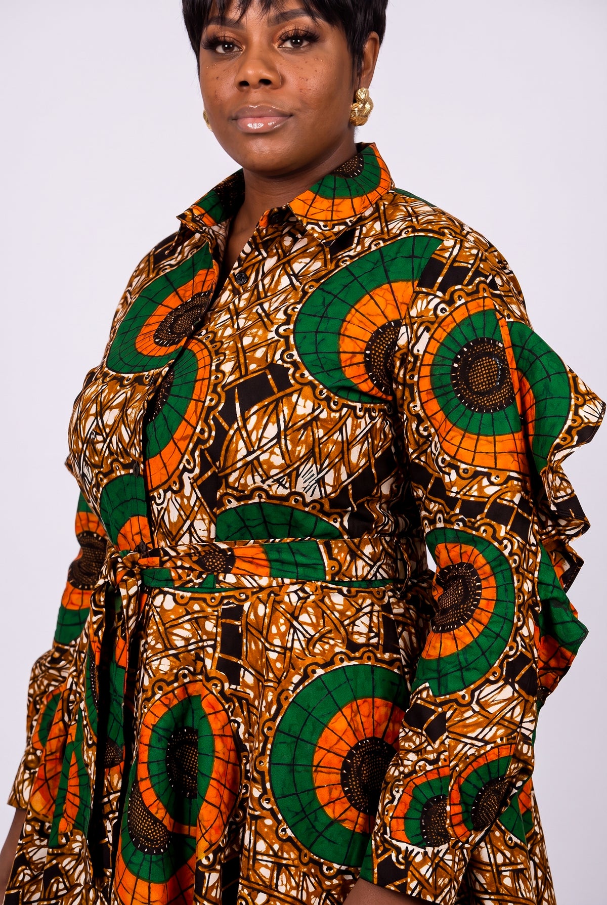 A woman wearing a long-sleeve collared shirt dress with a bold African wax print pattern in green, orange, brown, and black