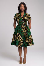 Front view of green, gold and teal African print midi wrap dress with both hands in side pockets