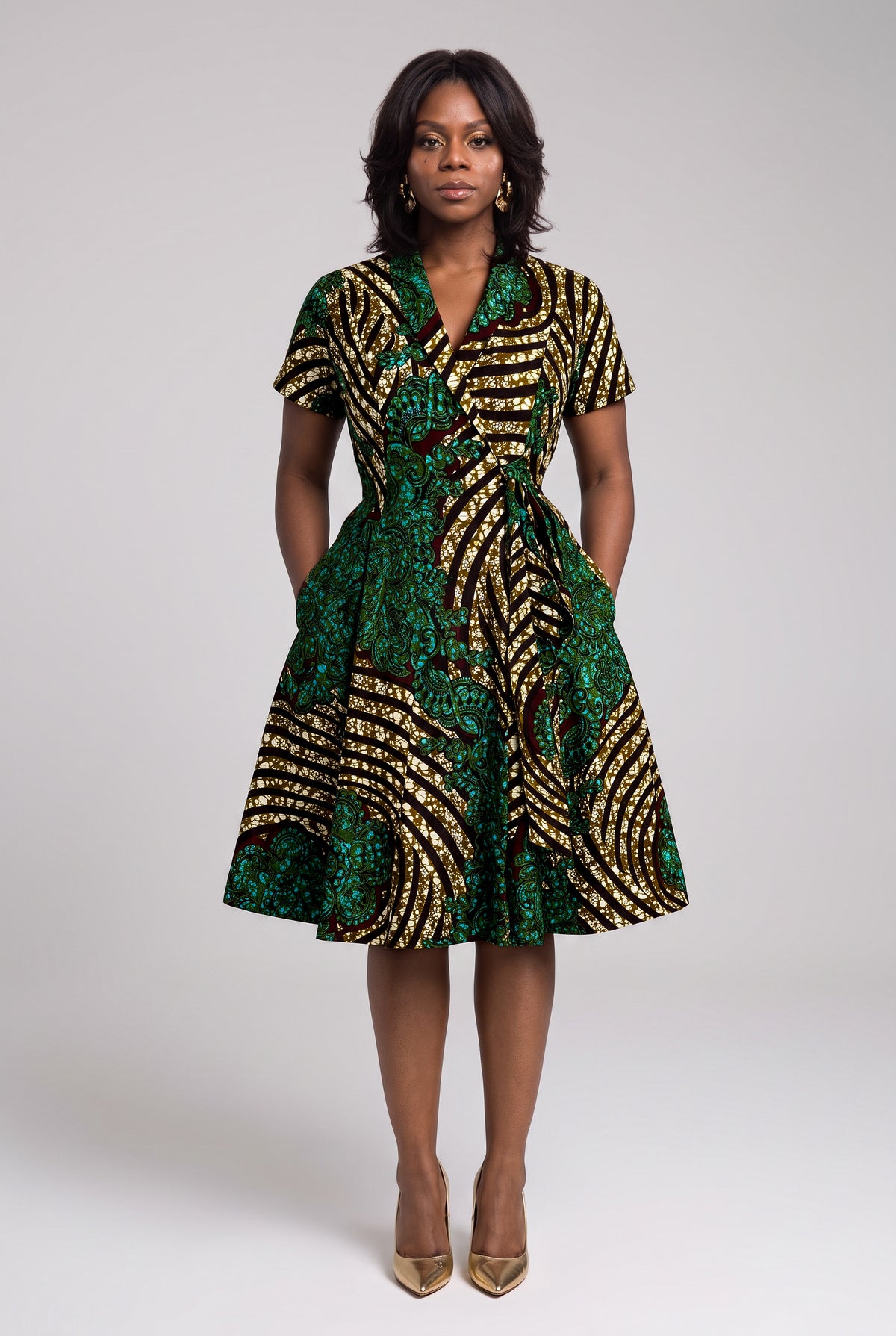 Front view of green, gold and teal African print midi wrap dress with both hands in side pockets