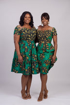 Two women modeling matching green African wax print dresses with black and gold floral patterns