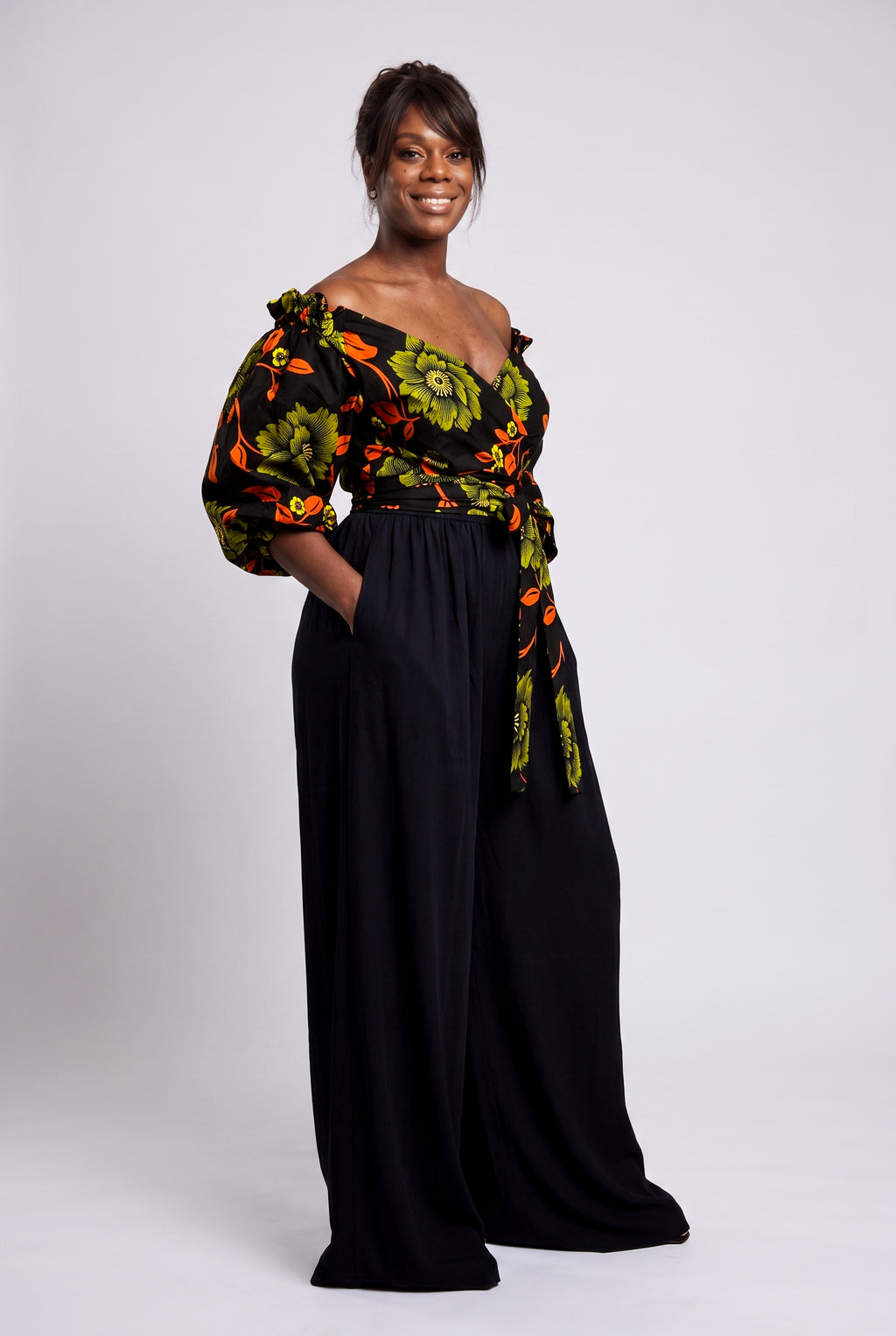 Side view of green and orange Ankara wrap top styled with black palazzo trousers