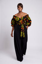 Model walking in Olive Oasis orange and green Ankara wrap top with black palazzo trousers